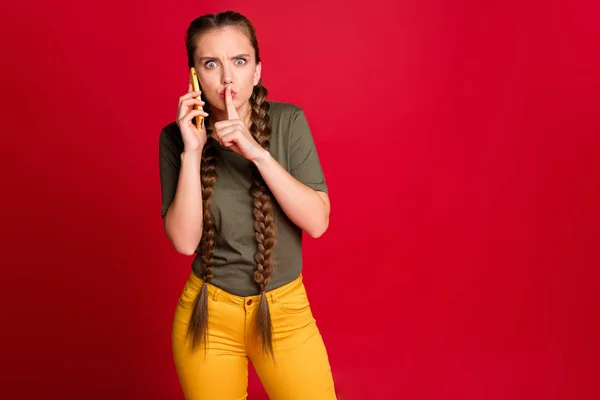 Foto de senhora bonita segurando as mãos do telefone falando com colegas de negócios dedo nos lábios discussão importante desgaste casual amarelo calças verde t-shirt isolado cor vermelha fundo — Fotografia de Stock