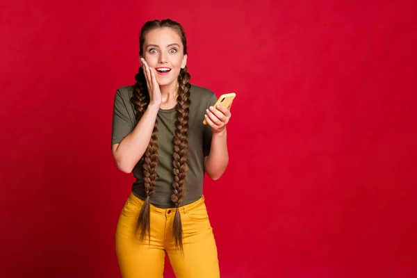 Foto van grappige dame met telefoon smart phone lezen positieve reacties voor instagram post dragen casual gele broek groen t-shirt geïsoleerde rode kleur achtergrond — Stockfoto