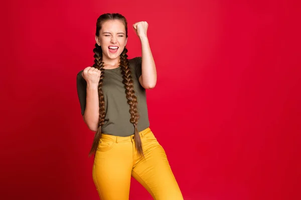 Photo of funny lady long warkocze podnoszące pięści w górę świętując najlepszy zwycięski zespół piłkarski niesamowity dzień nosić casual zielony t-shirt żółte spodnie odizolowane czerwony kolor tła — Zdjęcie stockowe