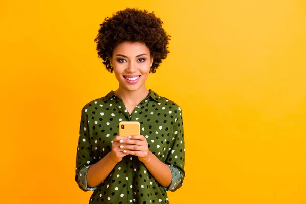 Portrait de positif gai afro américaine fille réseau social accro utilisateur tenir smartphone lire les médias sociaux nouvelles porter des vêtements élégants isolés sur fond de couleur brillance — Photo