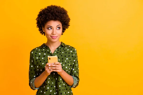 Foto di bella pelle scura divertente ondulato signora tenere le mani del telefono leggere buone notizie giovani sguardo vuoto spazio annuncio indossare verde punteggiato camicia isolato giallo colore sfondo — Foto Stock