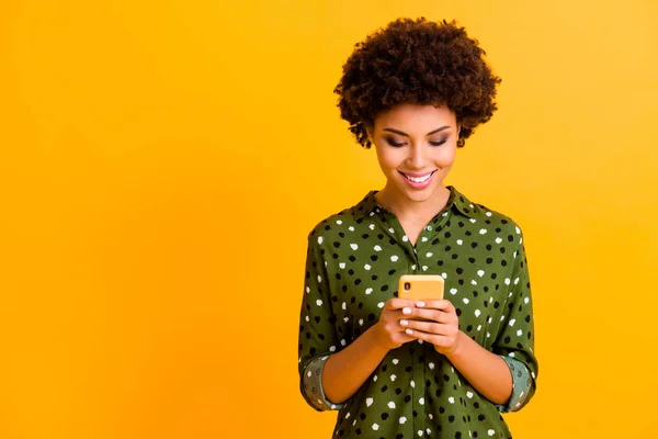 Foto de hermosa piel oscura dama ondulada sosteniendo las manos del teléfono leyendo buenas noticias de la juventud toothy sonriente desgaste verde punteado camisa aislado color amarillo fondo — Foto de Stock