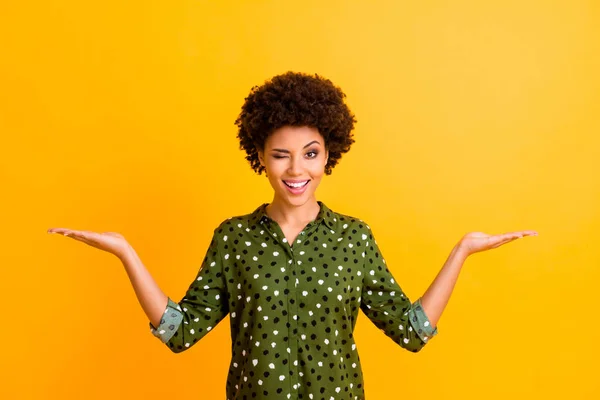Retrato de animado alegre afro-americano menina segurar mão desfrutar de anúncios promo exibir descontos de vendas piscar de olhos usar roupa elegante isolado sobre fundo de cor amarela — Fotografia de Stock