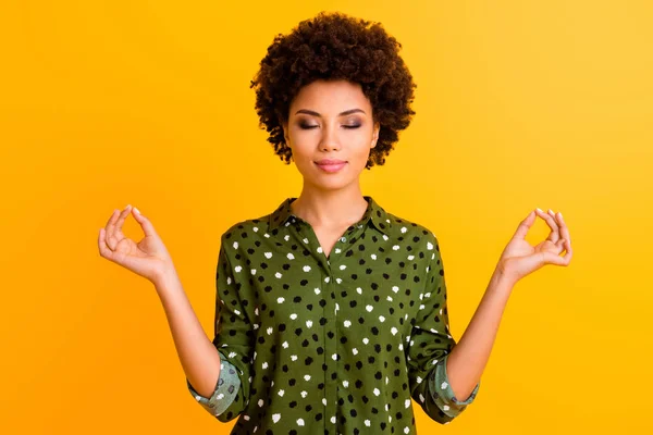 Photo of beautiful dark skin lady eyes closed holding hands om position meditating morning relaxation wear green dotted shirt isolated yellow color background