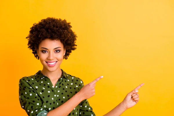 Φωτογραφία από αστείο toothy σκούρο δέρμα κυματιστή κυρία δείχνουν δάχτυλα κενό χώρο συμβουλεύει τον αγοραστή νέο προϊόν χαμηλή τιμή φορούν μοντέρνα πράσινο διάστικτη μπλούζα πουκάμισο απομονωμένο κίτρινο χρώμα φόντο — Φωτογραφία Αρχείου