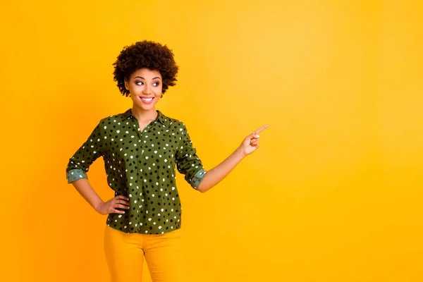 Photo of amazing dark skin curly lady indicating finger empty space advising buyer new product wear trendy green dotted shirt blouse pants isolated yellow color background — Stock Photo, Image