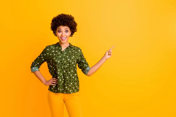 Foto di sorprendente pelle scura ondulato signora direttore vendite indicando dito vuoto spazio consigliare acquirente novità usura moda verde punteggiato camicia camicetta pantaloni isolato colore giallo sfondo — Foto Stock