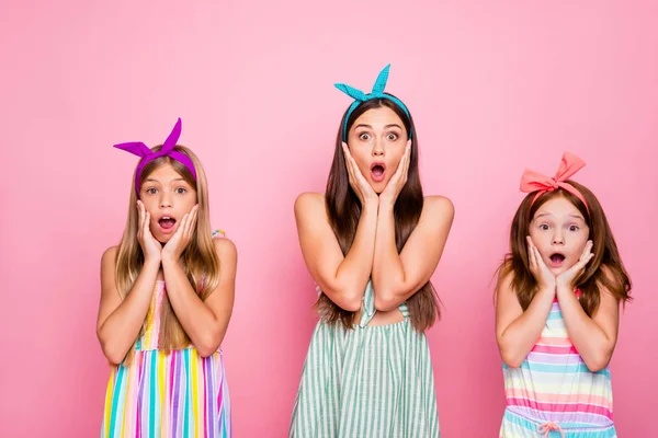 Porträtt av imponerade flickor med färg pannband skrikande omg röra sina kinder höra nyheter bär klänning kjol isolerad över rosa bakgrund — Stockfoto