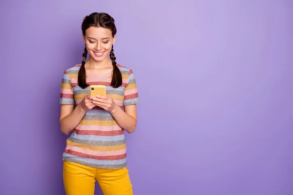 Foto van mooie dame met telefoon armen lezen van nieuwe post positieve reacties dragen casual gestreepte t-shirt geel broek geïsoleerde pastel paarse kleur achtergrond — Stockfoto