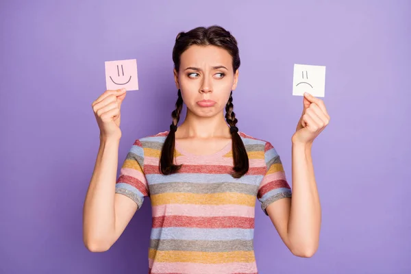 Photo of gloomy lady holding paper emoticons good and bad mood prefer negative emotions awful day wear casual striped t-shirt isolated pastel purple color background — Stock Photo, Image