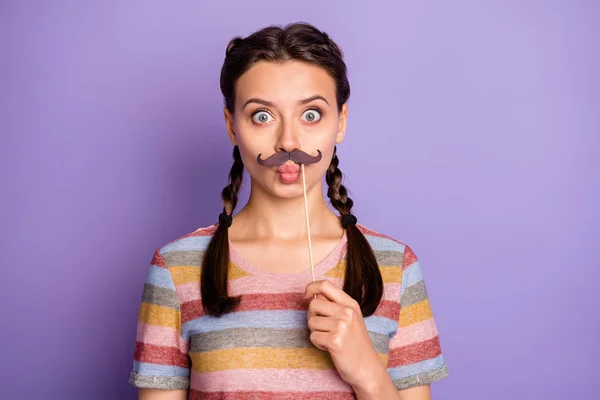 Foto av ganska barnslig humör dam håller falska papper mustasch nära munnen agerar som kille karneval parti bära casual randig t-shirt isolerad pastell lila färg bakgrund — Stockfoto