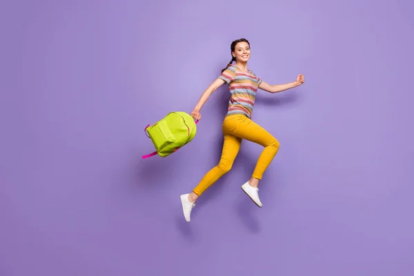 Full size photo of crazy excited lady jumping high carry school green rucksack rushing home after lessons wear casual striped t-shirt yellow pants isolated purple color background