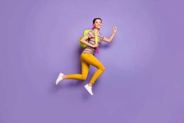 Teljes test profil fotó funky hölgy jumping nagy horderejű iskolatáska rohanó haza órák befejezni viselni alkalmi csíkos póló sárga nadrág elszigetelt lila színű háttér — Stock Fotó