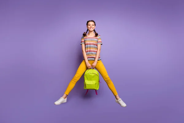 授業後のクールなスクールバッグ気楽な気分でハイジャンプファンキーな女性の完全な長さの写真カジュアルストライプTシャツ黄色のズボン孤立紫色の背景を身に着けています — ストック写真