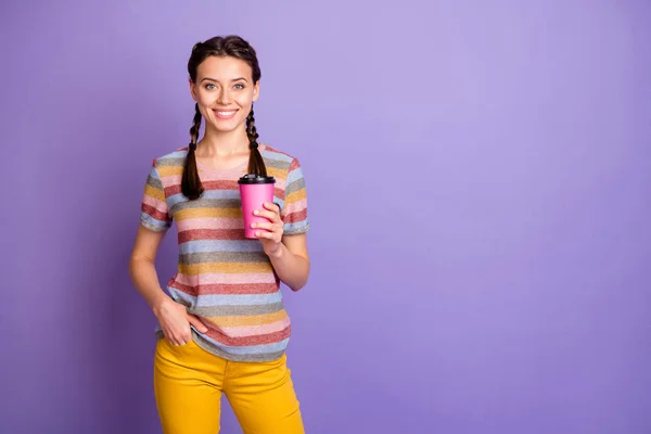 照片上，一位滑稽女士拿着粉红纸杯热咖啡，走在大街上，身穿休闲条纹T恤，背景是淡紫色 — 图库照片