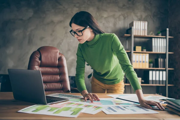 Foto av vackra företag dam titta bärbar skärm papper statistik på bordet analysera pengar inkomst stående nära stol slitage specs grön polotröja gula byxor moderna kontor — Stockfoto