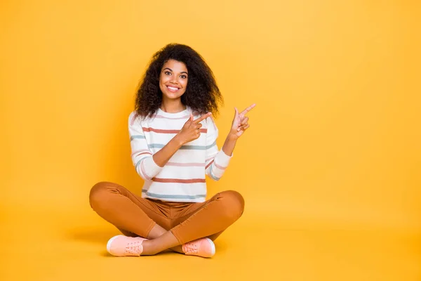 Retrato de ella ella agradable atractivo contenido alegre alegre alegre chica de pelo ondulado sentado en pose de loto señalando a un lado consejos aislados en brillante brillo vivo vibrante color amarillo fondo — Foto de Stock