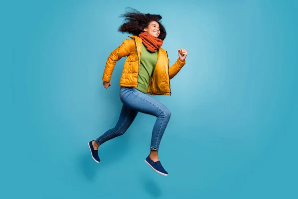 Full size profiel foto van vrij donkere huid dame springen hoog haasten winkel kortingen dragen overjas jeans groene trui sjaal geïsoleerde blauwe kleur achtergrond — Stockfoto