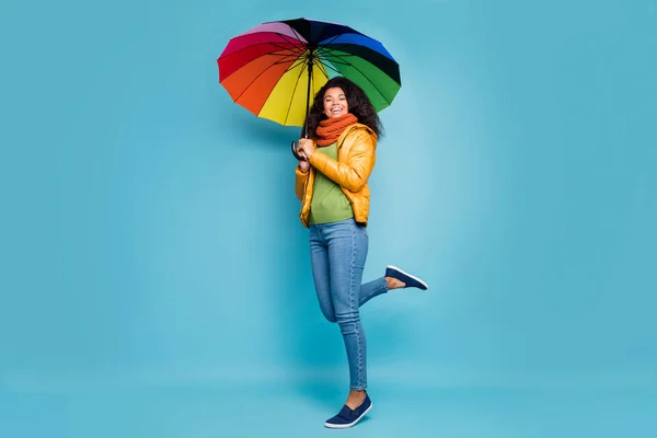 Volledige lichaam foto van vrij donkere huid golvende dame houden parasol goed weer lopen straat toeristische dragen gele jas jeans groene trui gebreide sjaal geïsoleerde blauwe kleur achtergrond — Stockfoto