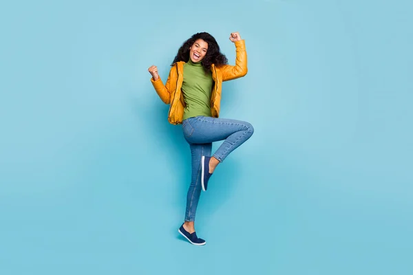 Full length foto di sorprendente pelle scura riccia signora estatica bene caldo autunno tempo camminare strada usura giallo primavera cappotto jeans verde pullover isolato blu colore sfondo — Foto Stock