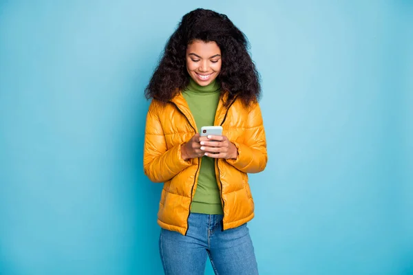 Fotografie okouzlující tmavé kůže dáma drží telefon ruce kontrolu následovníci nosí žluté jaro kabát džíny svetr izolované modré barvy pozadí — Stock fotografie