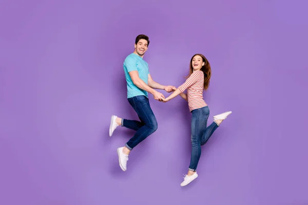 In voller Größe Profilfoto von flippigen zwei Personen Kerl Dame springen hoch halten Hände Spaß Gefühle tragen lässige blau gestreifte T-Shirts Jeans Schuhe isoliert lila Farbe Hintergrund — Stockfoto