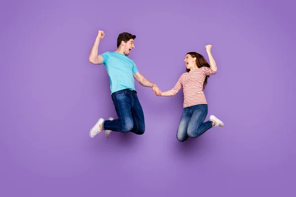Полное фото тела смешных двух человек парень женщина прыгает высоко держа руки радуясь экстатическим достижением носить повседневные синие полосатые футболки джинсы обувь изолированы фиолетовый цвет фона — стоковое фото