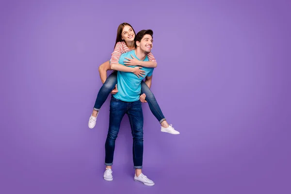 Plná délka fotografie dvou bezstarostných lidí chlap nesoucí Lady piggyback veselý volný čas letní víkend nosit ležérní stylové modré pruhované trička džíny izolované fialové barvy pozadí — Stock fotografie