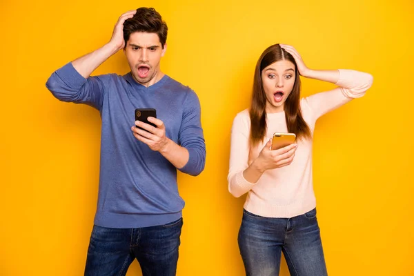 Impresionante blogger pareja romántica uso smartphone leer noticias grito wow omg desgaste azul suéter rosa vaqueros aislados sobre fondo de color amarillo — Foto de Stock