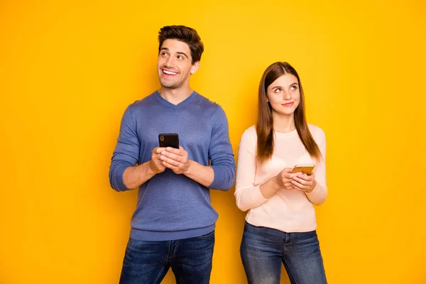 Retrato de inspirado dois estudantes pessoas casal uso smartphone pensar pensamentos que post na rede social usar azul pulôver rosa jeans jeans jeans isolado sobre fundo de cor amarela — Fotografia de Stock