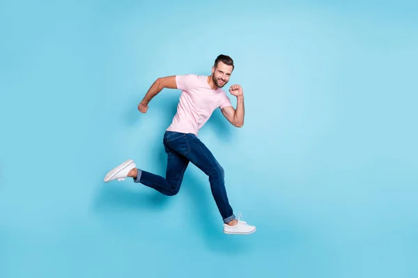 In voller Länge Profilfoto von attraktiven Kerl springen hohe sportliche Wettbewerbe Teilnehmer tragen lässige rosa T-Shirt Jeans Turnschuhe isoliert blaue Farbe Hintergrund — Stockfoto