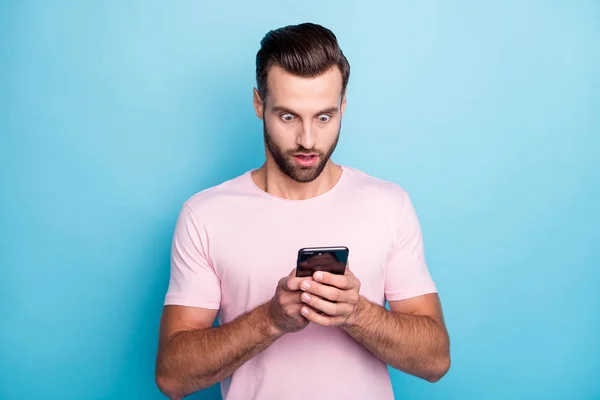 Photo de gars attrayant tenant les mains du téléphone bouche ouverte lecture de mauvaises nouvelles commentaires négatifs post adeptes portent casual t-shirt rose isolé fond de couleur bleue — Photo