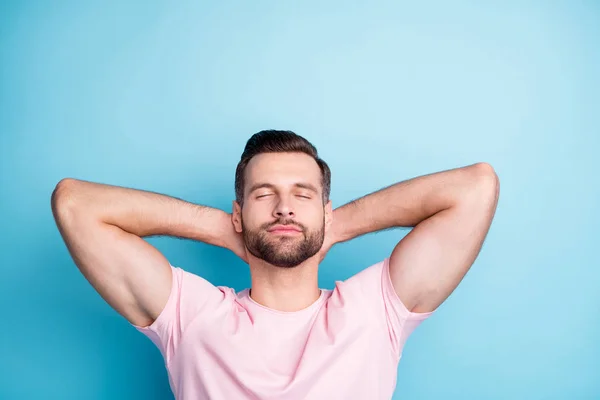 Фото привлекательного парня, держащего руки за голову глаза закрыты насладиться удивительным выходной день расслабляющий носить повседневную розовую футболку изолированный синий цвет фона — стоковое фото