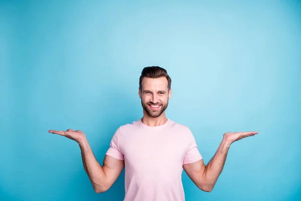 Photo d'attrayant macho gars tenant les paumes ouvertes présentant de nouveaux produits conseillant les meilleurs prix de vente bas porter casual t-shirt rose isolé fond de couleur bleue — Photo