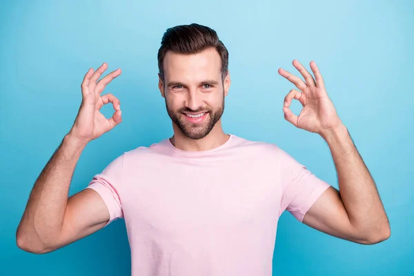 Close up foto di attraente ragazzo che si tiene per mano mostrando okey simboli che esprimono accordo dentino sorridente usura casual rosa t-shirt isolato colore blu sfondo — Foto Stock