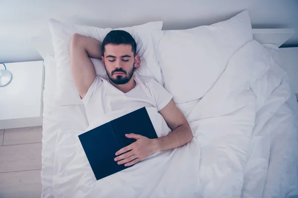 In alto sopra alto angolo vista ritratto del suo bel ragazzo barbuto attraente sdraiato sul letto bianco riposo addormentato pacificamente addormentato tenendo in mano libro di notte tarda sera casa camera appartamento al coperto — Foto Stock