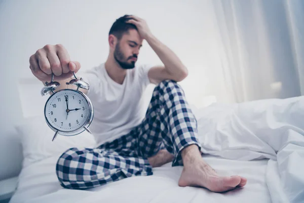 Portrait of his he nice attractive sad lazy tired bearded guy sitting on bed holding in hand alarm clock suffering at night late evening home dark room flat house indoors — Stock Photo, Image