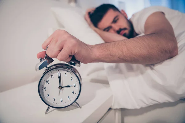 Close-up retrato dele ele agradável atraente irritado cansado cara deitado na cama segurando na mão despertador que sofre de doença à noite tarde à noite casa hotel branco quarto apartamento — Fotografia de Stock