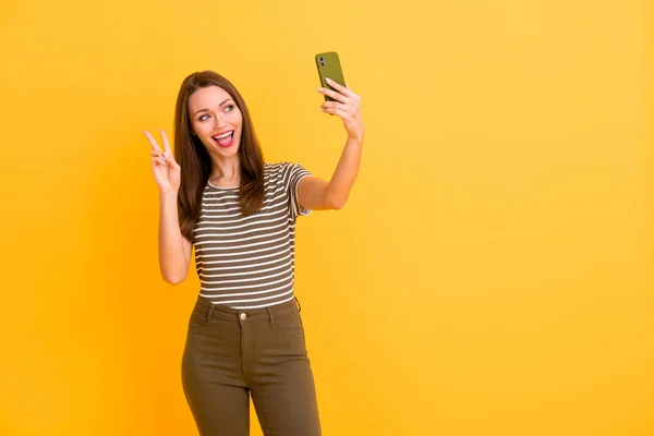 Retrato de alegre chica positiva blogueando en el viaje de vacaciones de primavera hacer selfie en el teléfono celular mostrar v-signos de desgaste traje de buen aspecto aislado sobre brillo color fondo — Foto de Stock