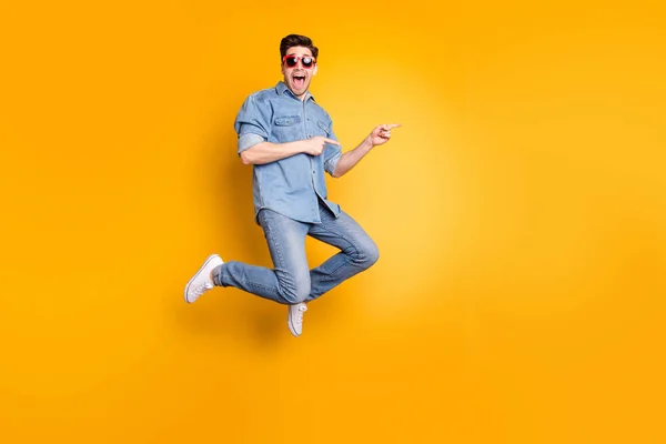 Взгляд в полный рост на симпатичного привлекательного и веселого веселого парня, прыгающего в сторону, показывая рекламные советы, изолированные на ярком светящемся ярко-желтом фоне — стоковое фото