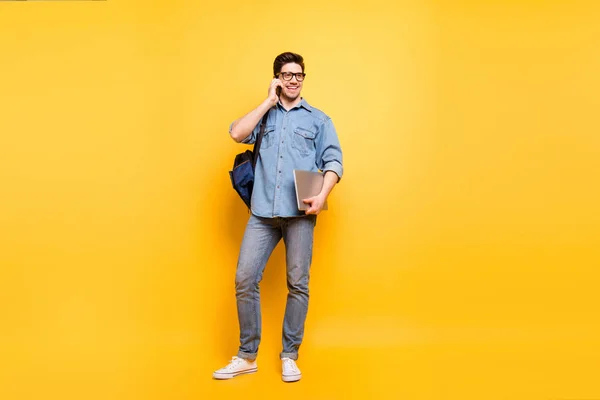 Volledige lichaamslengte foto van vrolijke positieve tand stralende man met laptop in de hand spreken per telefoon in witte sneakers geïsoleerde levendige kleur achtergrond — Stockfoto