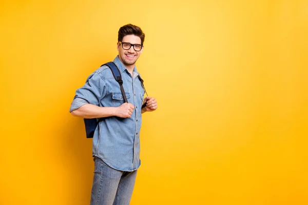 Foto de homem positivo alegre perto do espaço vazio com mochila atrás das costas isolado fundo de cor brilhante vestindo óculos — Fotografia de Stock