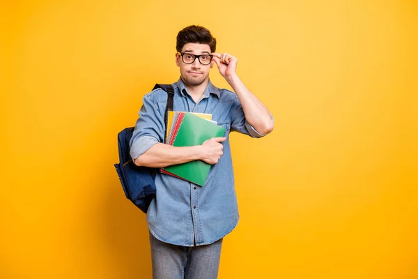 Fotografie plachý váhavý dobrý chlap nosí brýle s batohem vzadu a ruce drží copybooks izolované živé barvy žluté pozadí — Stock fotografie