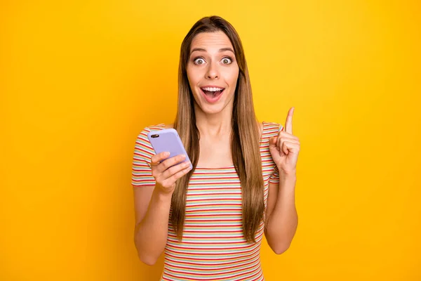 Photo of pretty crazy lady trzymać telefon ręce myśleć nad nowym tekstem pomysł kreatywny osoba podnieść palec wskazujący powietrze nosić casual pasiasty t-shirt odizolowany żółty kolor tła — Zdjęcie stockowe