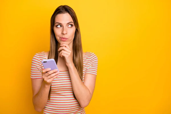 Foto van vrij slimme dame houden telefoon handen denken over nieuwe instagram post tekst idee creatieve persoon hand op kin dragen casual gestreepte t-shirt geïsoleerde gele kleur achtergrond — Stockfoto