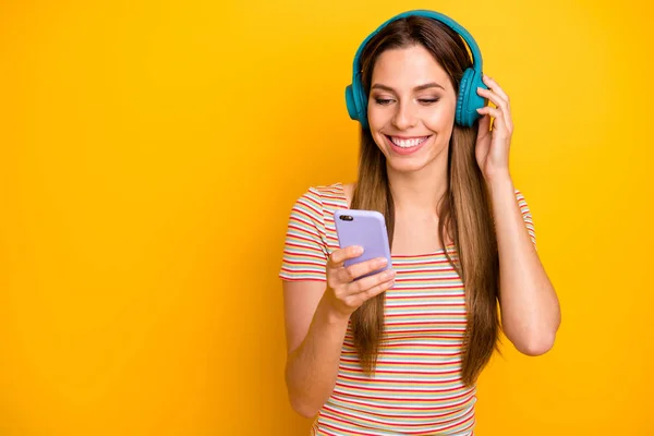 Zdjęcie śmieszne ładna pani trzymać telefon słuchać muzyki fajne bezprzewodowe słuchawki włączanie utworu nosić casual paski t-shirt odizolowany żółty kolor tła — Zdjęcie stockowe