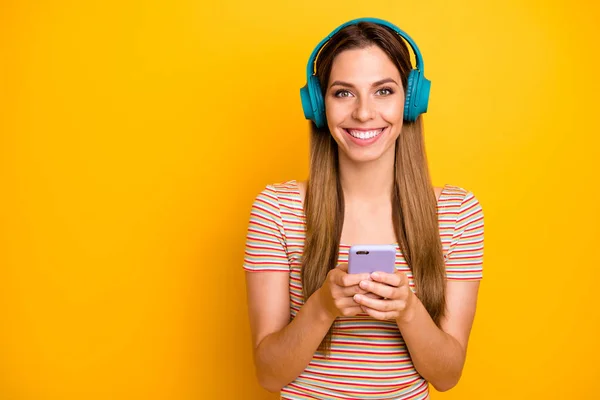 Zdjęcie pięknej pani trzymającej telefon słuchać muzyki w chłodnych bezprzewodowych słuchawek wybierając następną piosenkę nosić casual paski t-shirt odizolowany żółty kolor tła — Zdjęcie stockowe