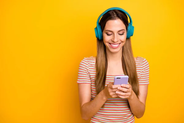 Foto de una hermosa dama sosteniendo el teléfono escuchar música en auriculares inalámbricos frescos elegir siguiente canción usar casual rayas camiseta aislada de color amarillo de fondo — Foto de Stock