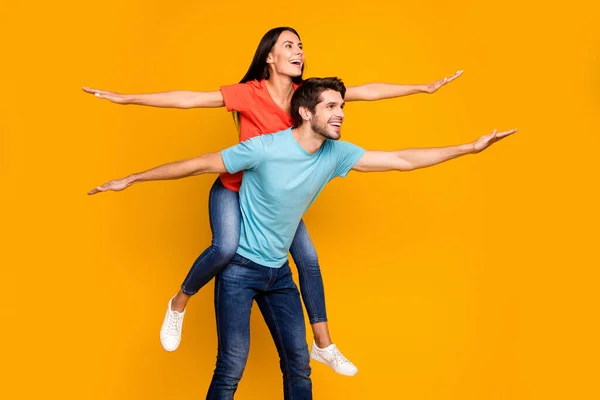 Profil fotografie legrační chlap nést dáma piggyback strávit léto spolu šíří ruce jako křídla nosit ležérní stylové modré oranžové trička džíny izolované žluté barvy pozadí — Stock fotografie