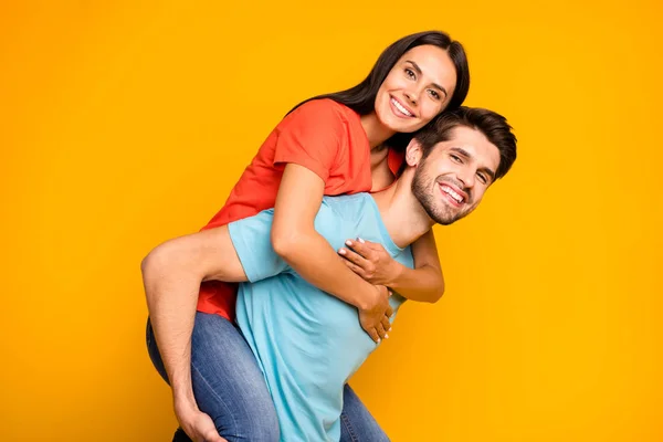 Профиль фото двух очаровательных людей парень, несущий леди piggyback встретить летние приключения вместе носить случайные стильные голубые оранжевые футболки джинсы изолированный желтый цвет фона — стоковое фото